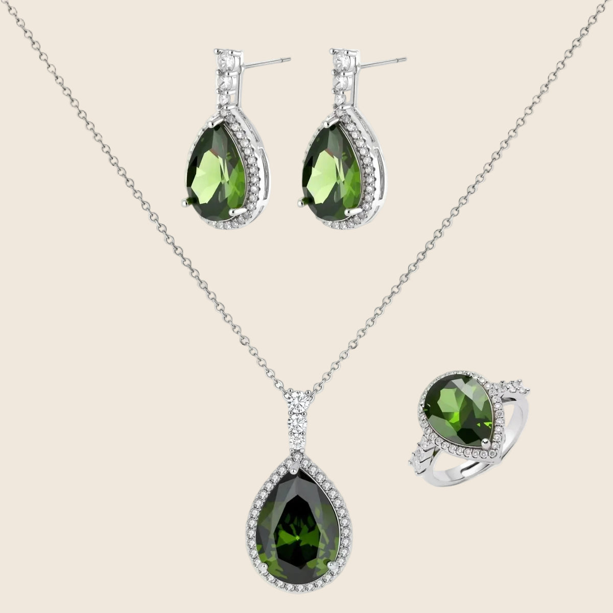 White gold plated jewelry set with green teardrop gemstones and cubic zirconia halos on cream background.
