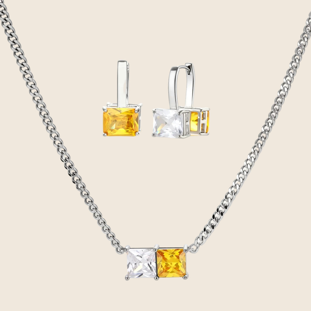 Silver curb-chain necklace and hoop drop earrings set with paired yellow and clear square zirconia stones.