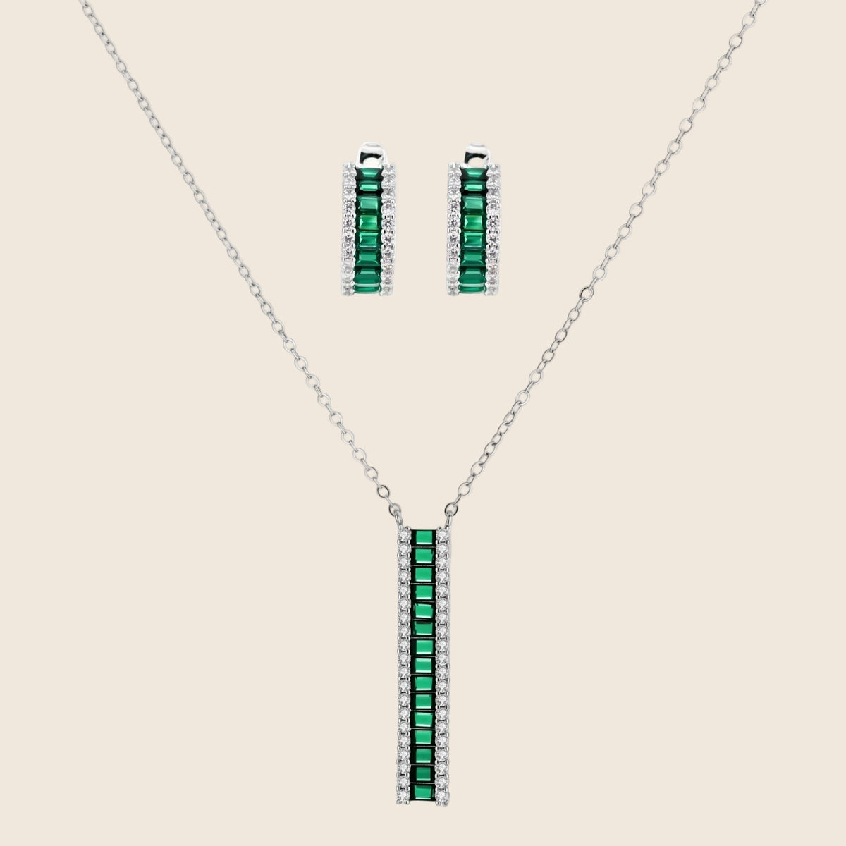 White gold plated jewelry set with emerald green rectangular stones and clear crystals in geometric rows on white background.