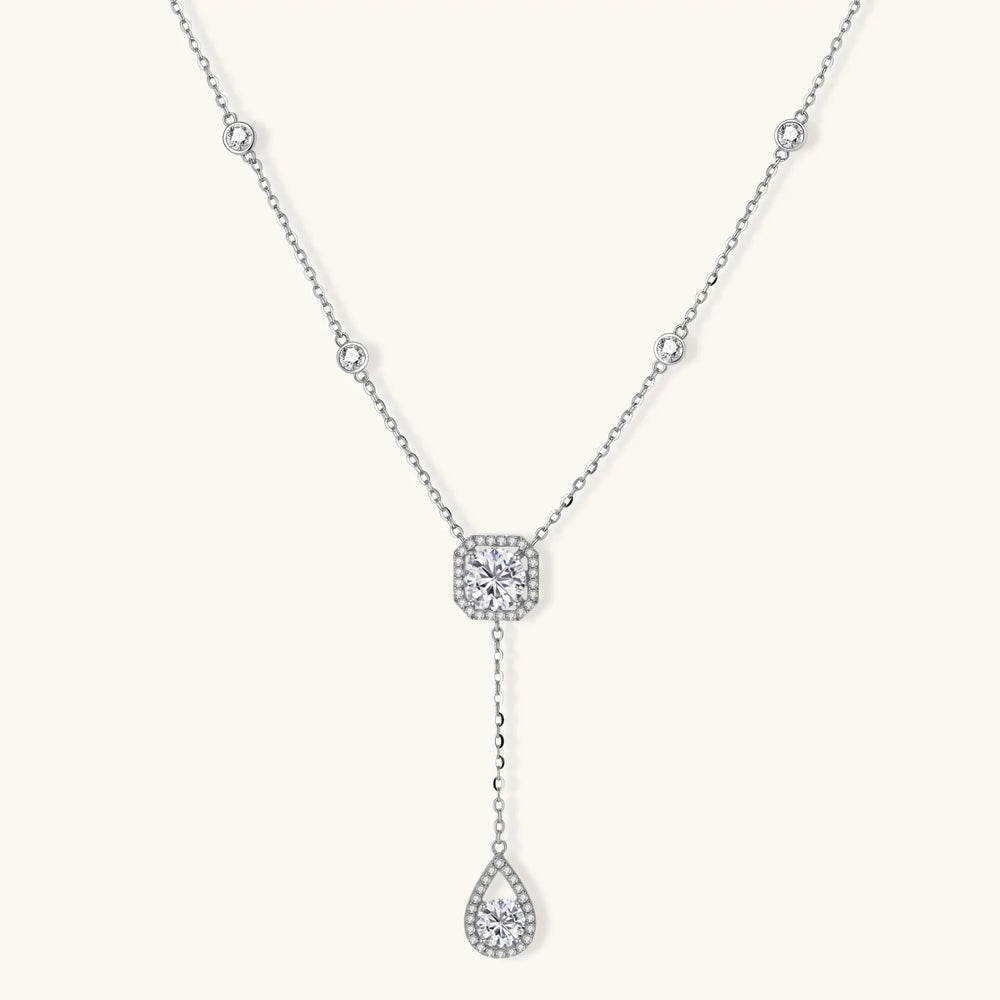 Sterling silver necklace with cushion-cut moissanite in halo setting and teardrop pendant, displayed on cream background.