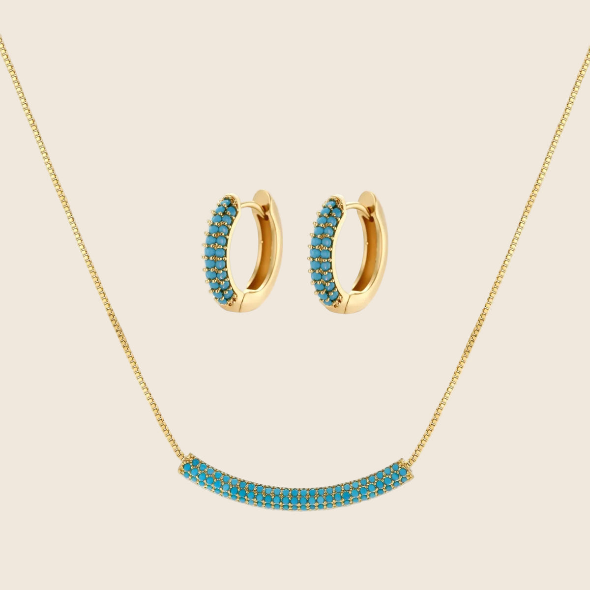 Gold-plated curved necklace and hoop earrings with turquoise cubic zirconia stones on white background.