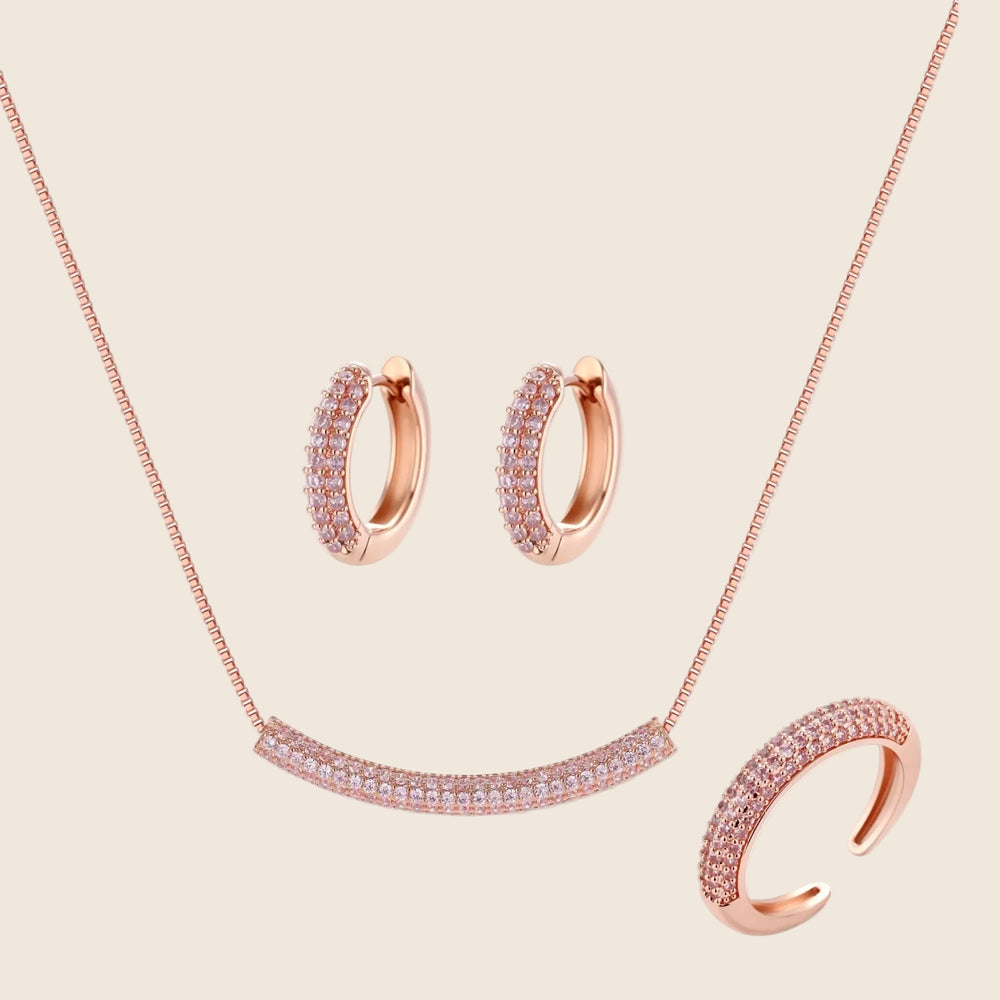 Rose gold pavé zirconia bar necklace, hoop earrings, and open ring set with pink stones on cream background.