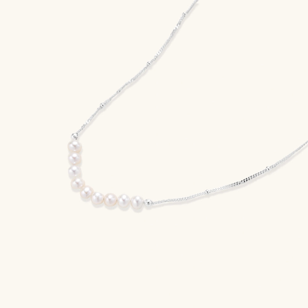 Delicate sterling silver chain necklace with small freshwater pearls arranged in a curved smile arc on cream background.