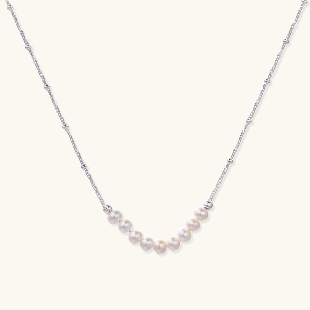 Delicate sterling silver chain necklace with small freshwater pearls arranged in a curved smile arc on cream background.