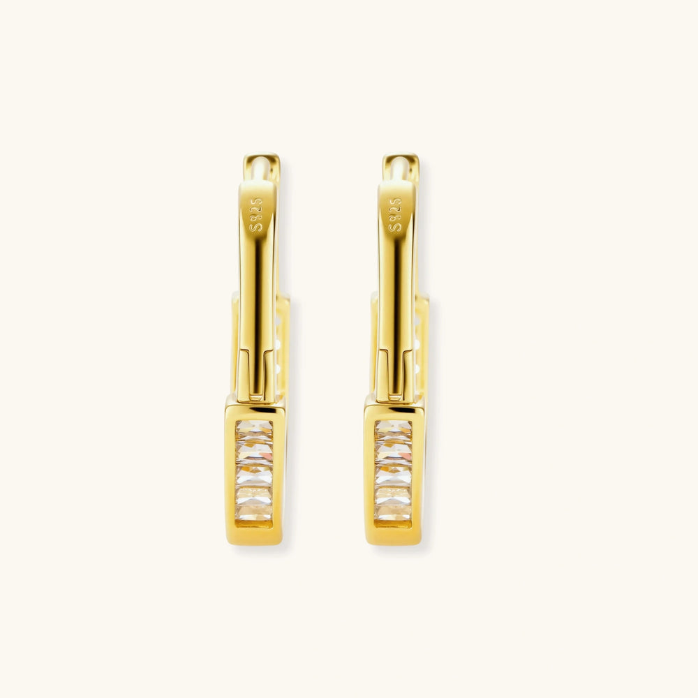Close-up of gold-plated sterling silver huggie hoop earrings featuring rectangular cubic zirconia stones on neutral background.