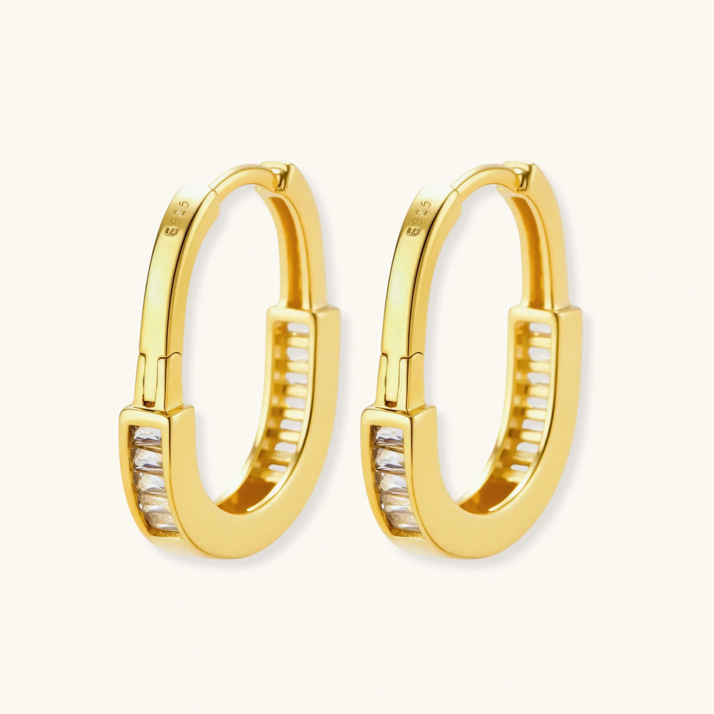 Close-up of gold-plated sterling silver huggie hoop earrings featuring rectangular cubic zirconia stones on neutral background.