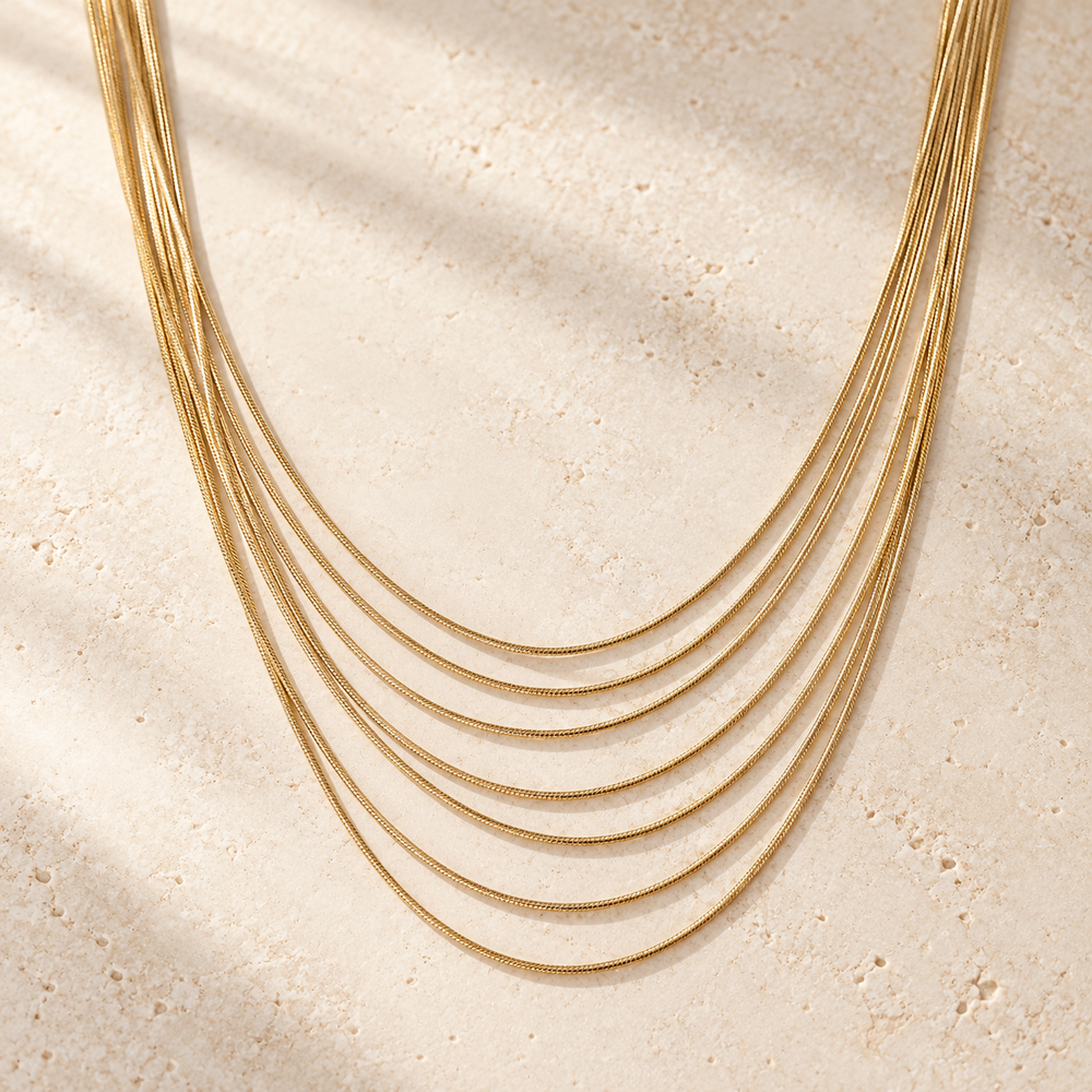 Golden Hour Layers Necklace with seven fine gold-tone chains arranged on ivory stone.