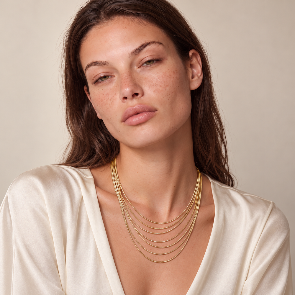 Model wearing the seven-layer Golden Hour Layers Necklace with an ivory blouse.
